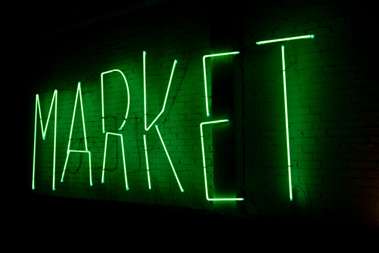 Vibrant green neon sign spelling 'MARKET' illuminating a brick wall at night.